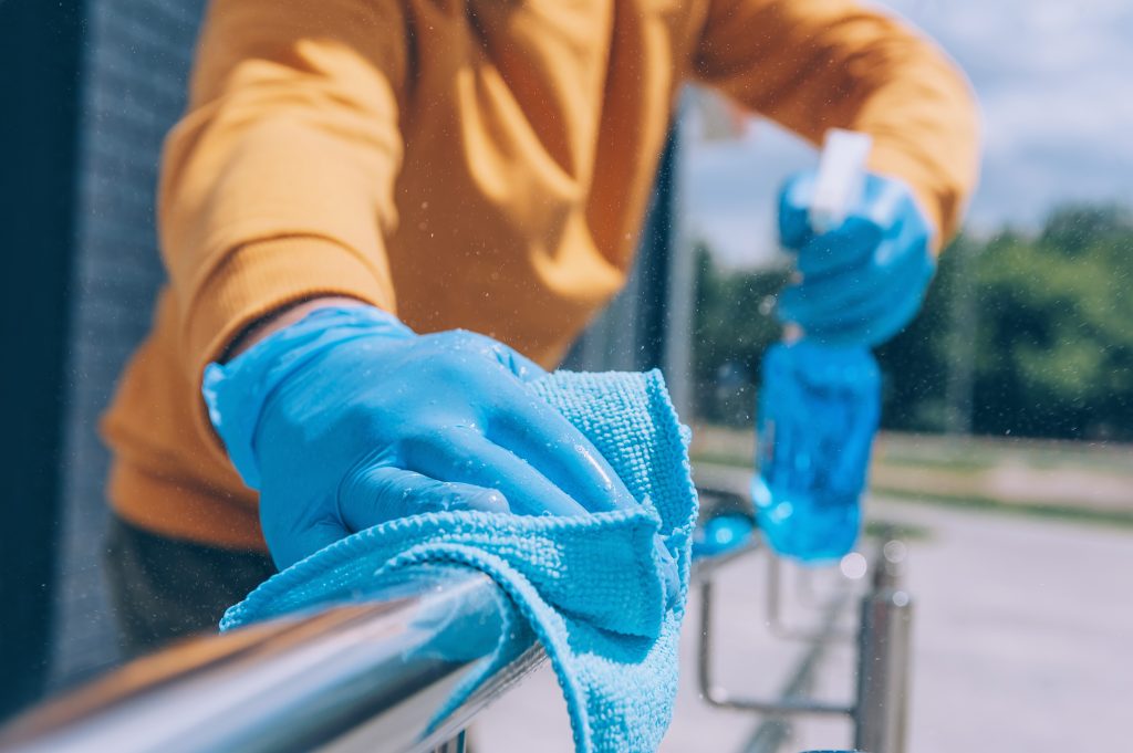 Un joven desinfecta una barandilla con un antiséptico azul y un trapo en la mano.